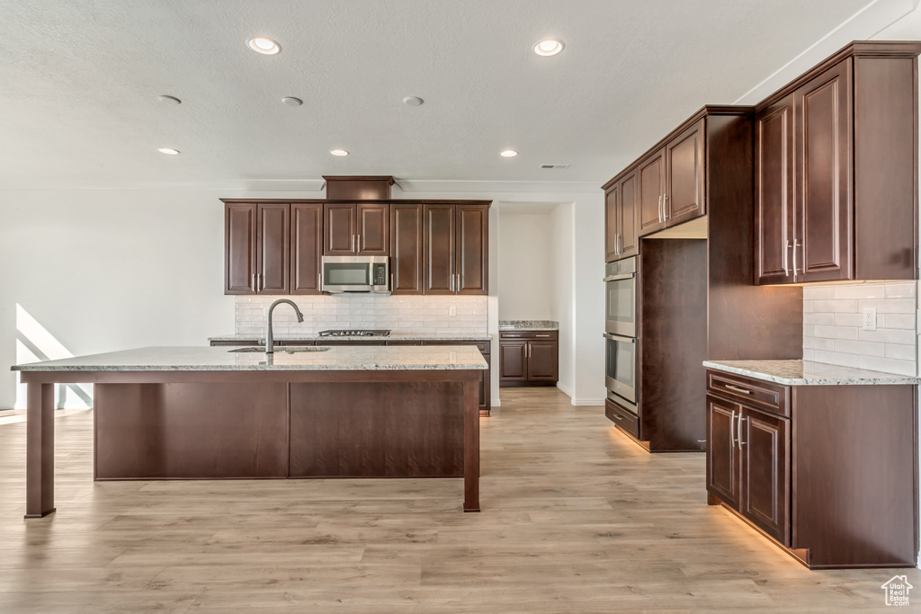 Kitchen featuring a breakfast bar, sink, tasteful backsplash, light hardwood / wood-style floors, and stainless steel appliances