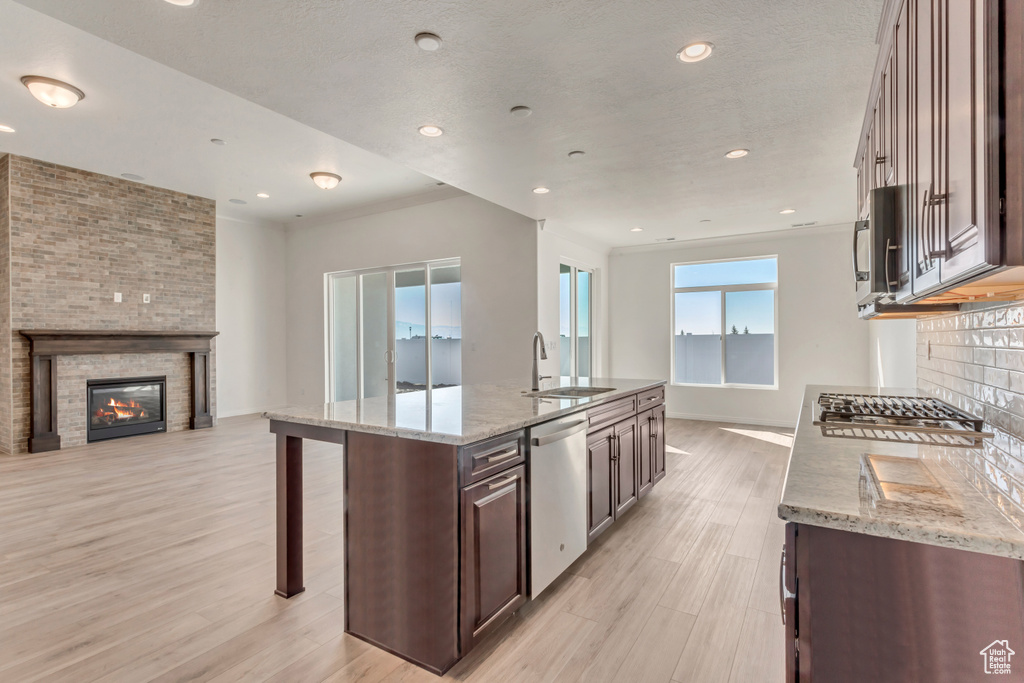 Kitchen featuring light wood-type flooring, stainless steel appliances, light stone counters, and a large fireplace