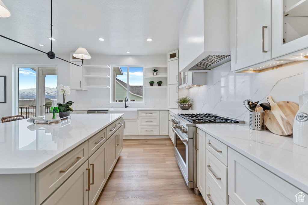 Kitchen with backsplash, light wood-type flooring, custom range hood, white cabinetry, and stainless steel stove