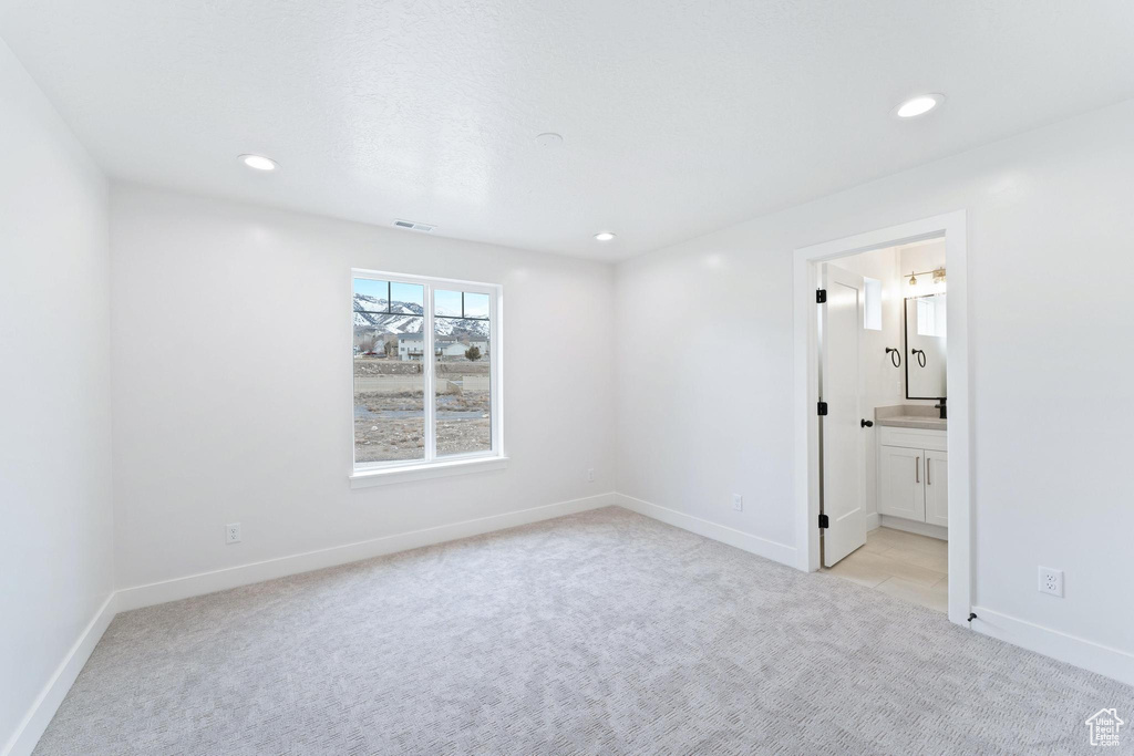Unfurnished bedroom featuring ensuite bathroom and light colored carpet