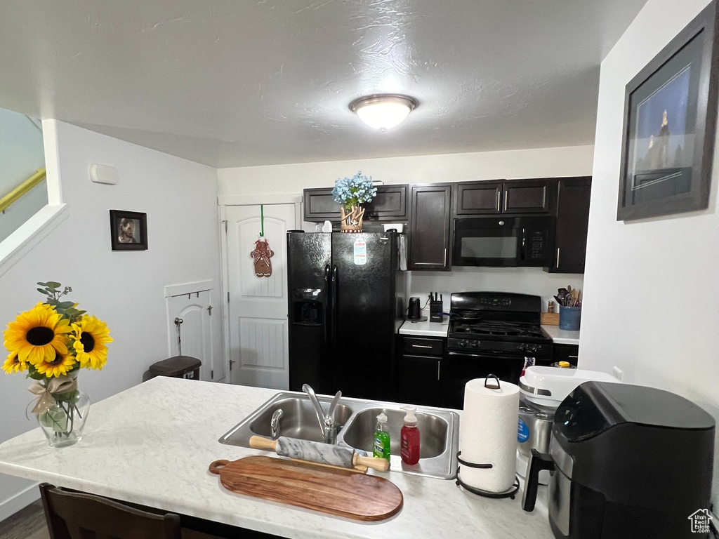 Kitchen with kitchen peninsula, dark wood-type flooring, sink, black appliances, and a kitchen bar