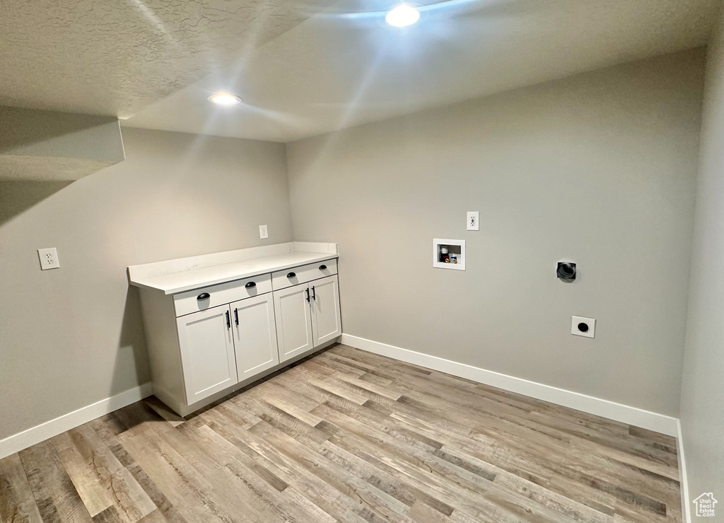 Laundry area featuring light hardwood / wood-style flooring, hookup for an electric dryer, a textured ceiling, and cabinets