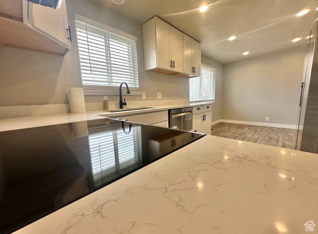 Kitchen with white cabinets, light hardwood / wood-style flooring, sink, and dishwasher