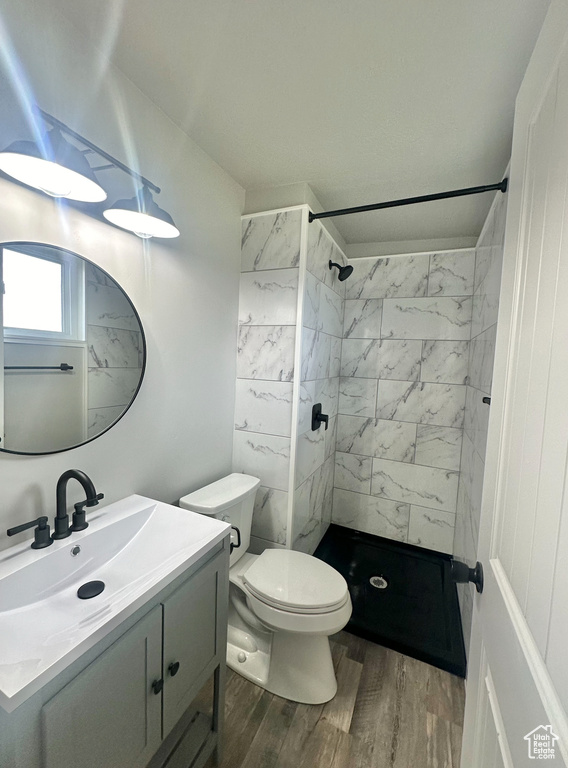 Bathroom featuring vanity, toilet, hardwood / wood-style floors, and a tile shower