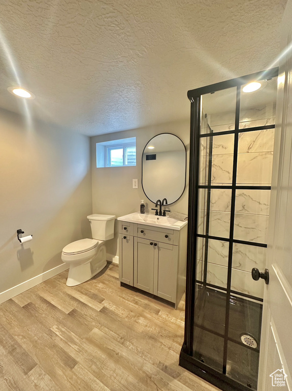 Bathroom with a textured ceiling, vanity, hardwood / wood-style floors, an enclosed shower, and toilet