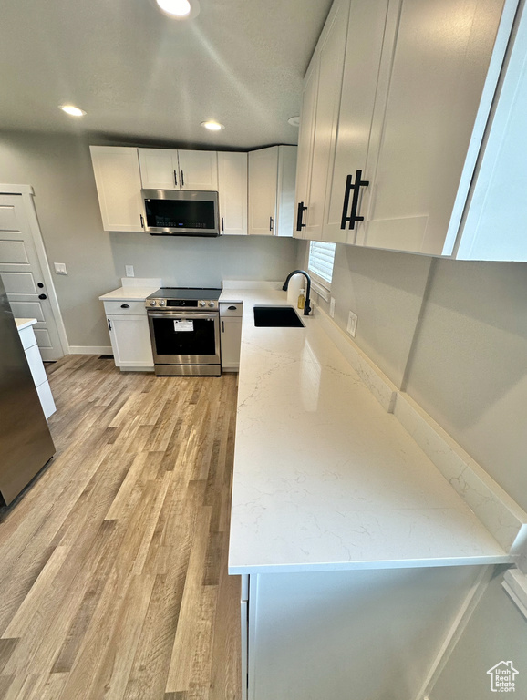 Kitchen with white cabinetry, light hardwood / wood-style flooring, sink, and appliances with stainless steel finishes