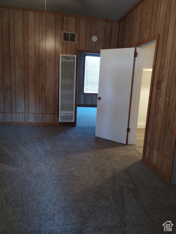 Unfurnished room featuring dark colored carpet and wooden walls