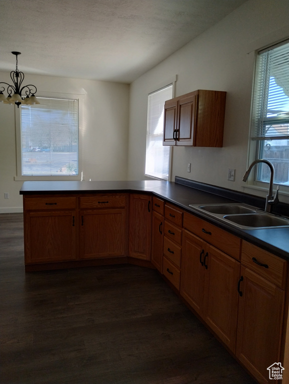 Kitchen with dark hardwood / wood-style flooring, sink, pendant lighting, a chandelier, and kitchen peninsula