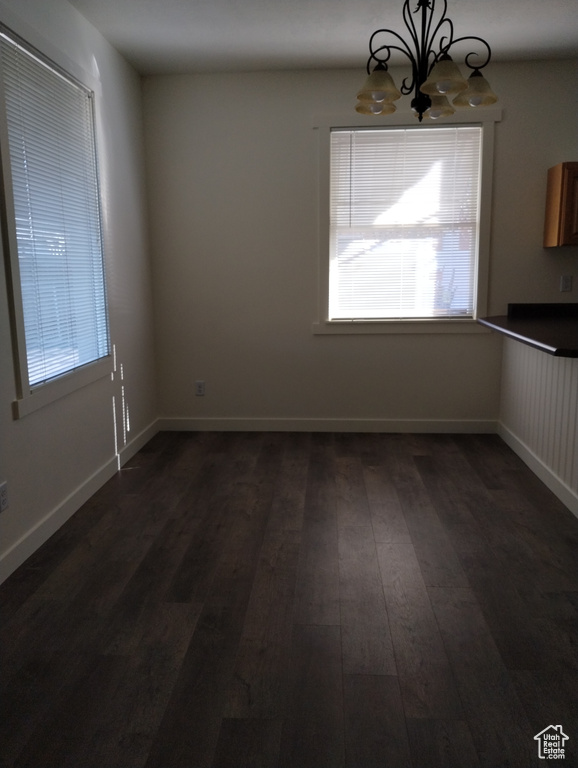 Spare room with dark hardwood / wood-style floors, an inviting chandelier, and a healthy amount of sunlight