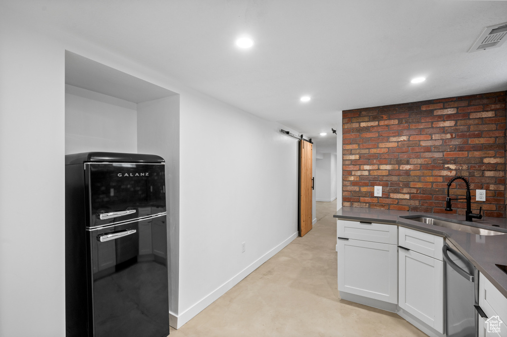 Kitchen featuring a barn door, brick wall, stainless steel dishwasher, sink, and white cabinetry