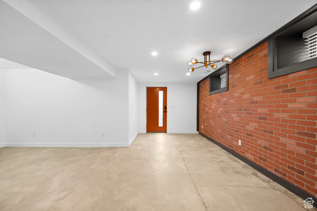Unfurnished room featuring an inviting chandelier and brick wall