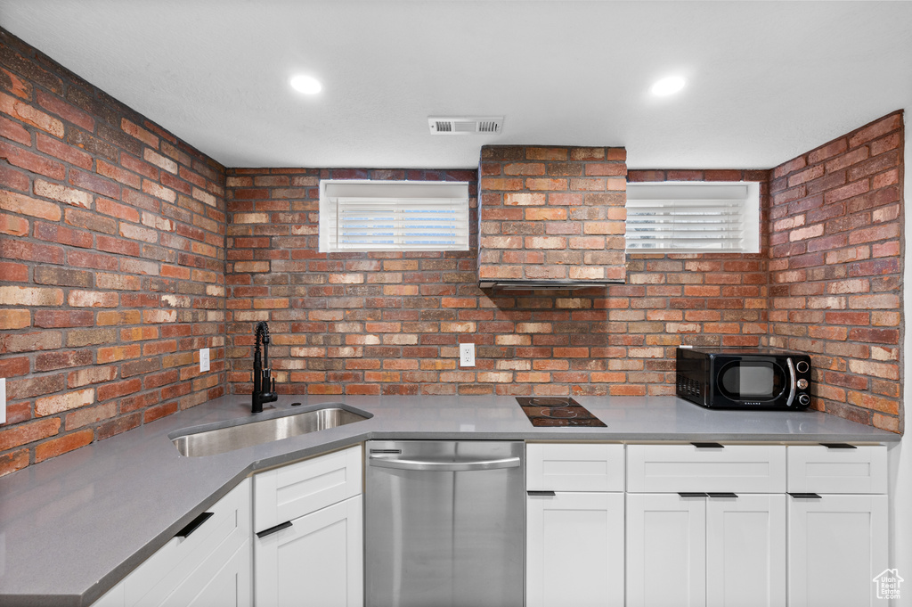 Kitchen with sink, dishwasher, white cabinets, and brick wall