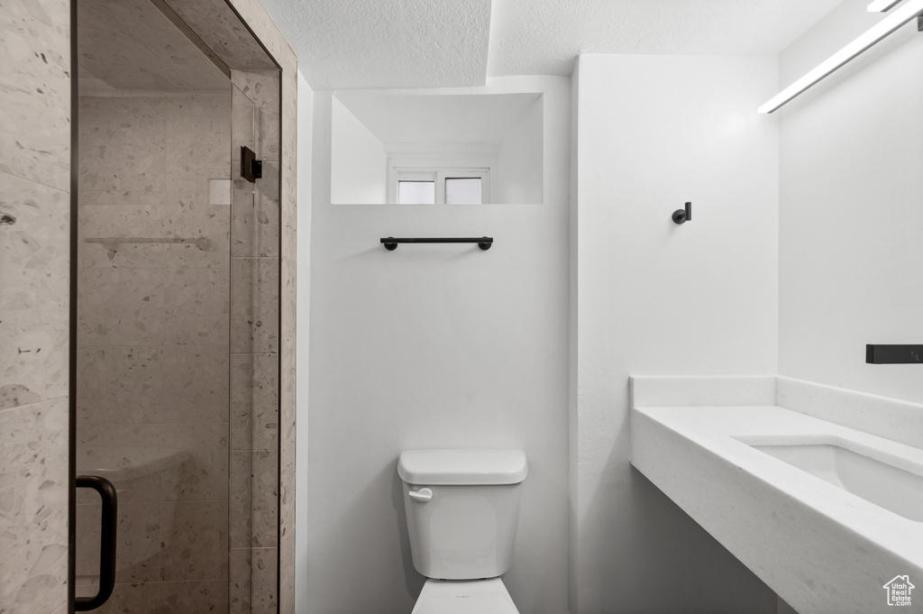 Bathroom featuring a shower with shower door, vanity, toilet, and a textured ceiling