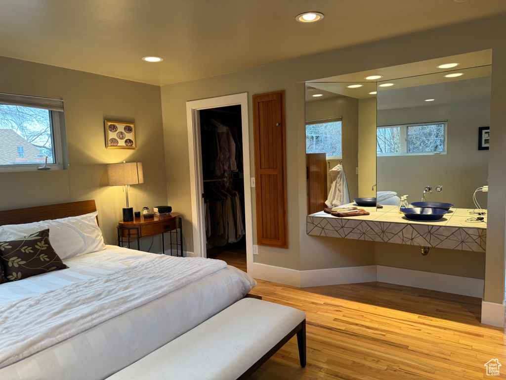 Bedroom with light hardwood / wood-style flooring, a walk in closet, multiple windows, and a closet