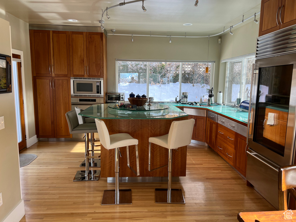 Kitchen with a kitchen island, light hardwood / wood-style flooring, stainless steel microwave, and track lighting