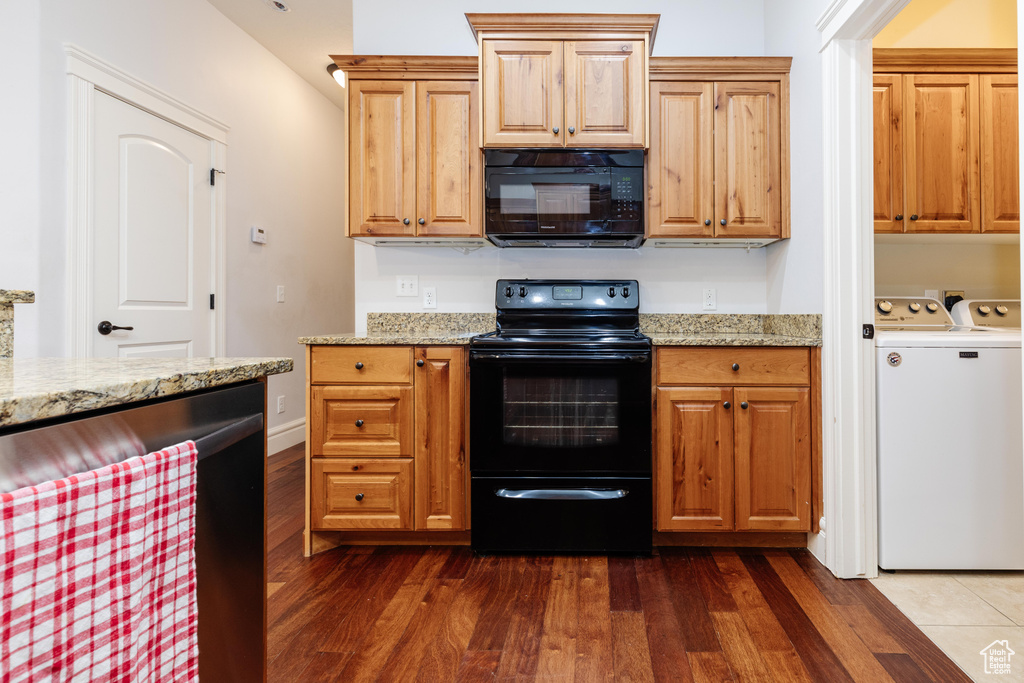Kitchen featuring separate washer and dryer, dark wood-type flooring, light stone counters, and black appliances