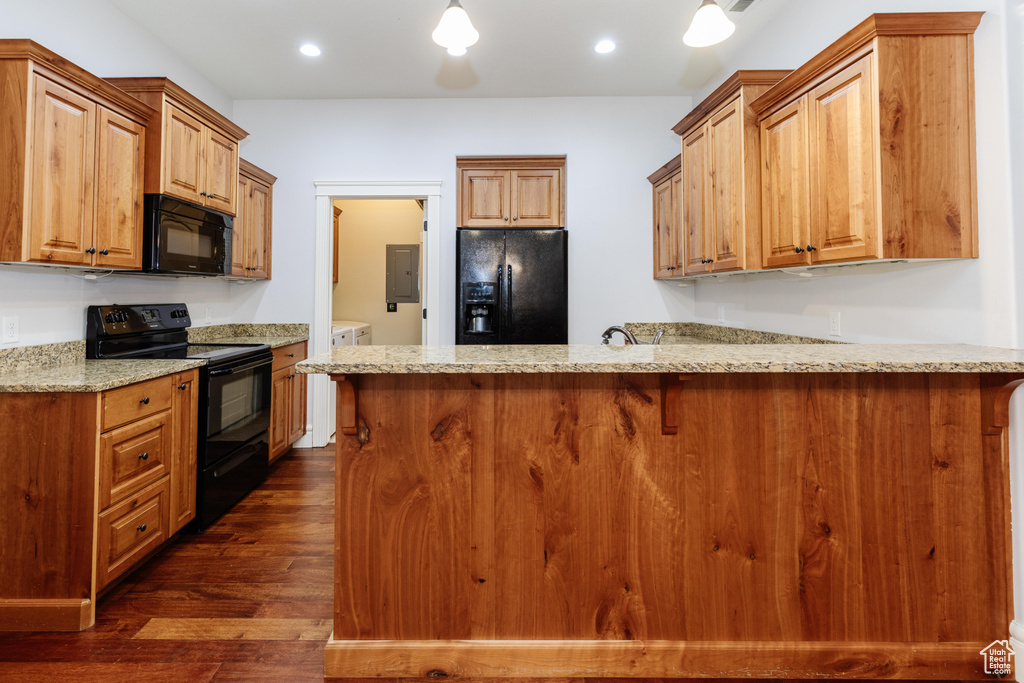 Kitchen with dark hardwood / wood-style floors, black appliances, light stone counters, and a breakfast bar area