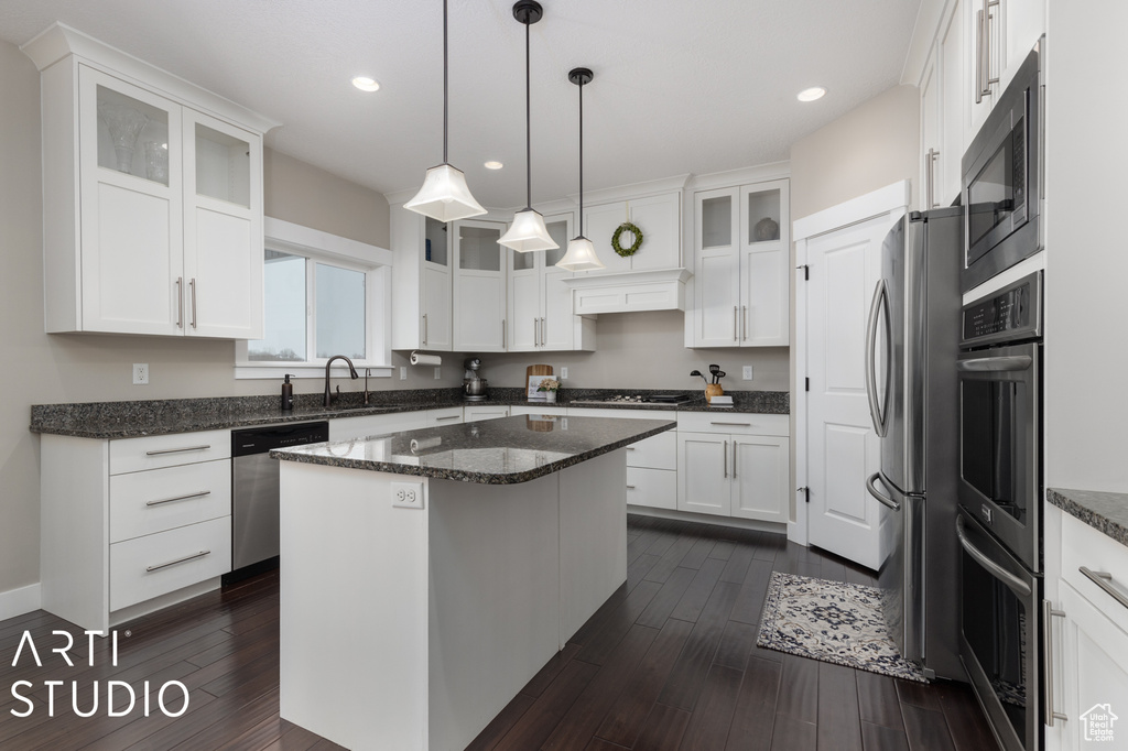 Kitchen featuring hanging light fixtures, appliances with stainless steel finishes, a center island, and dark stone countertops