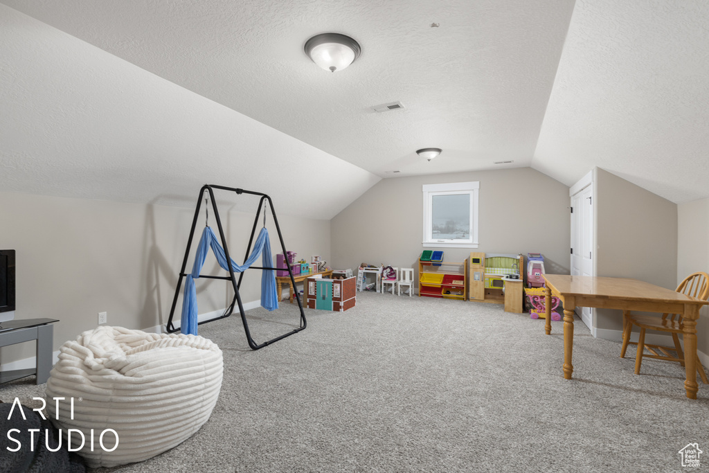Rec room featuring light colored carpet, a textured ceiling, and lofted ceiling