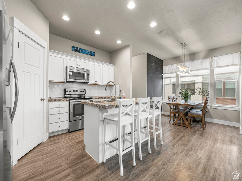 Kitchen featuring hardwood / wood-style floors, stainless steel appliances, white cabinets, hanging light fixtures, and sink