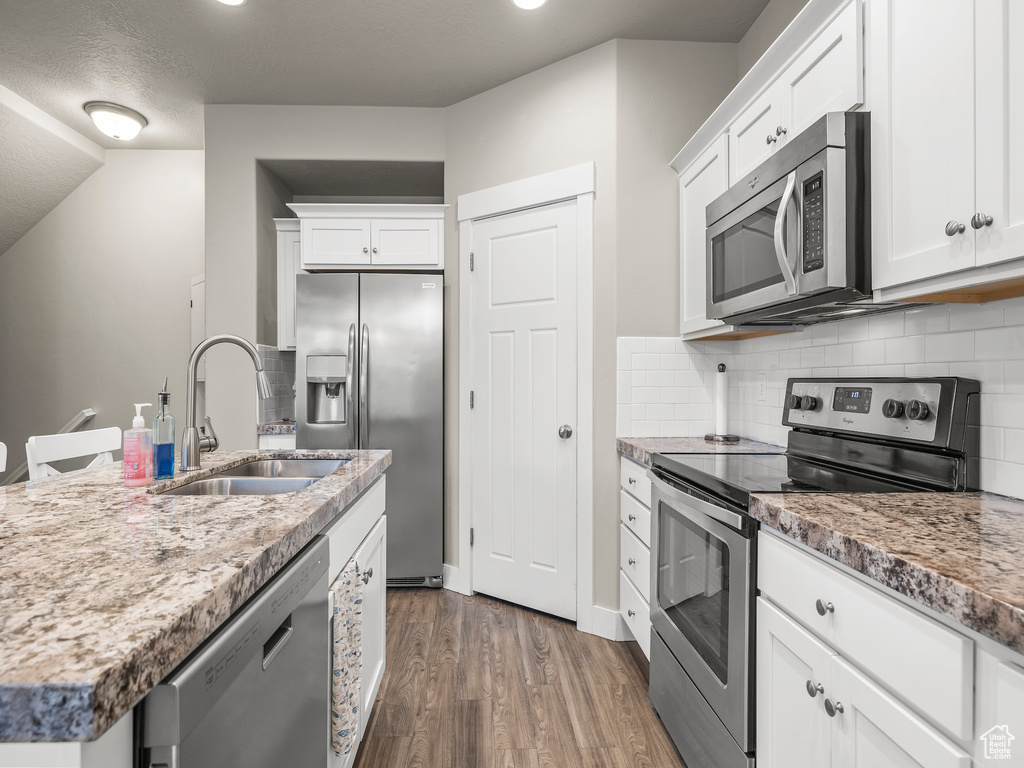Kitchen featuring dark wood-type flooring, stainless steel appliances, white cabinetry, tasteful backsplash, and sink