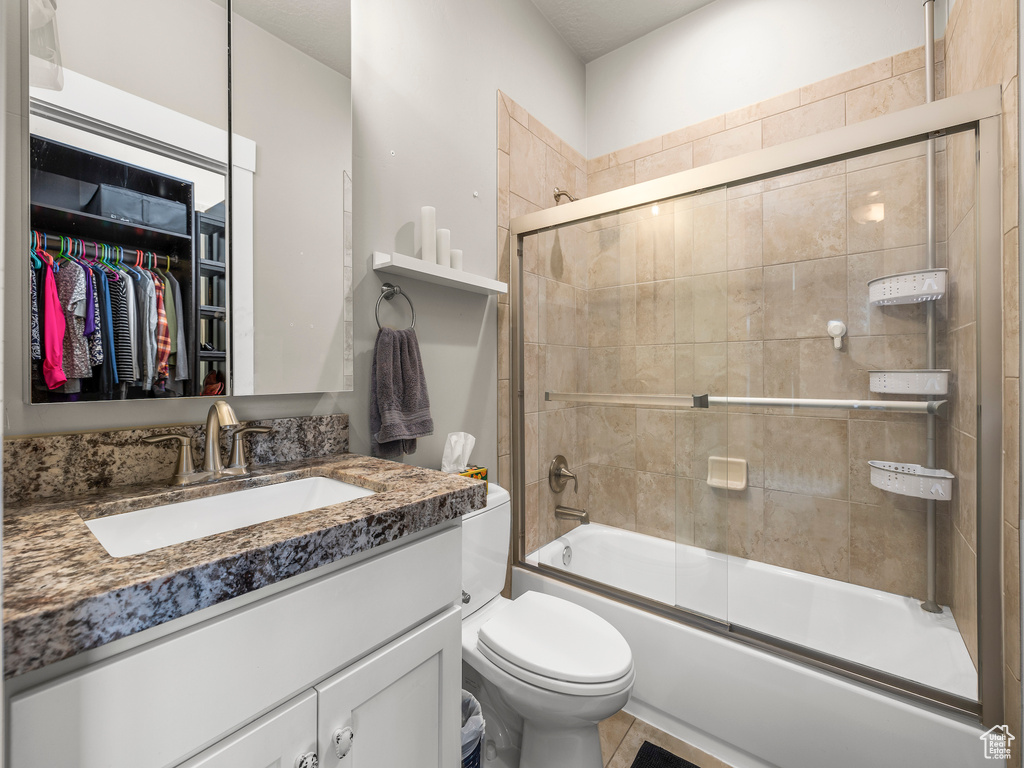 Full bathroom featuring bath / shower combo with glass door, toilet, tile floors, and vanity with extensive cabinet space