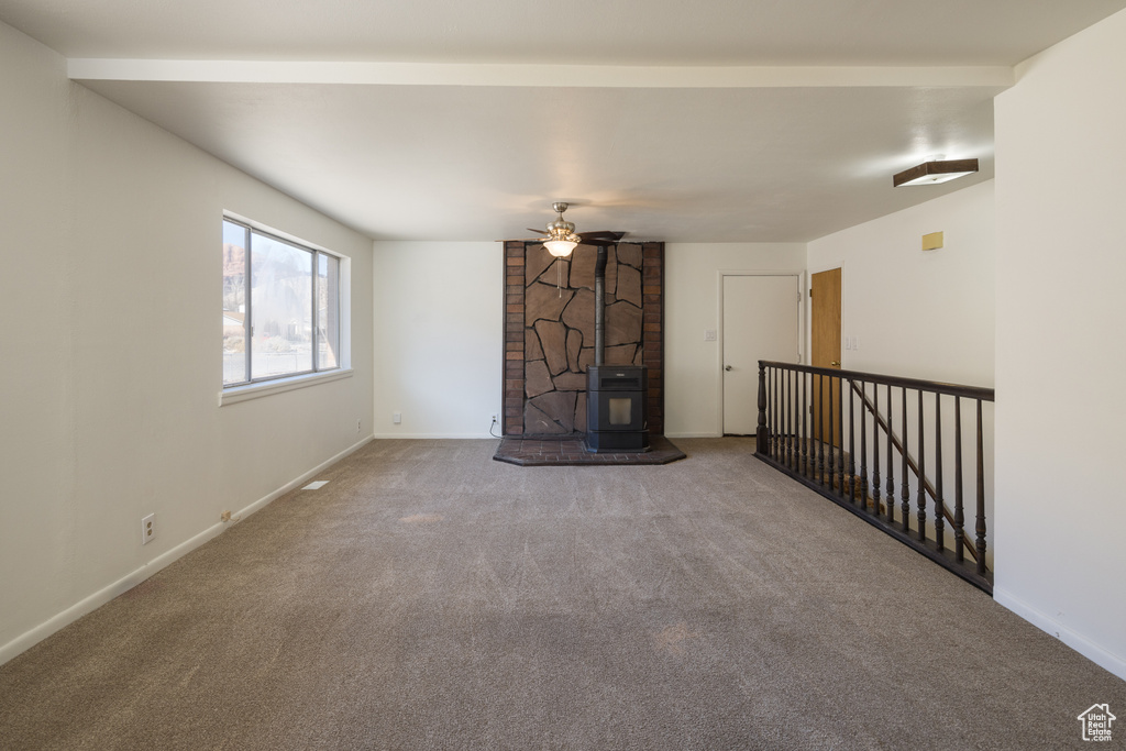 Unfurnished living room featuring carpet floors, ceiling fan, and a wood stove