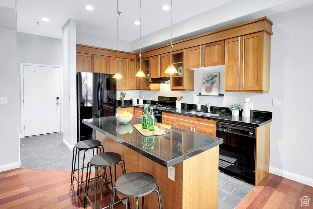 Kitchen featuring light wood-type flooring, a kitchen island, a breakfast bar, hanging light fixtures, and black appliances