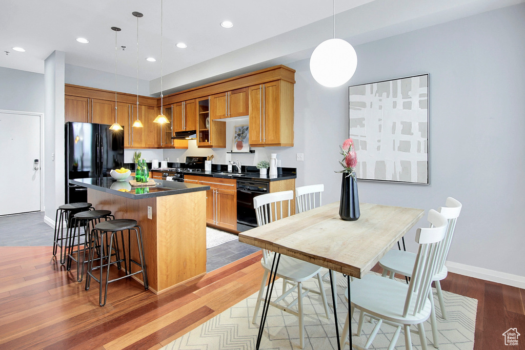 Kitchen featuring light hardwood / wood-style flooring, a kitchen island, black appliances, a kitchen bar, and hanging light fixtures