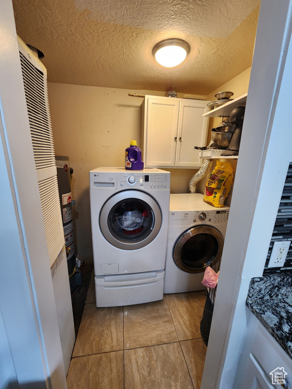 Clothes washing area with light tile floors, washing machine and dryer, a textured ceiling, and cabinets
