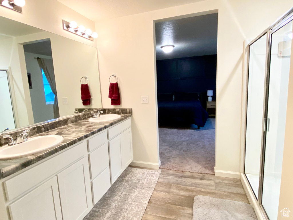 Bathroom featuring a shower with shower door, wood-type flooring, oversized vanity, and double sink