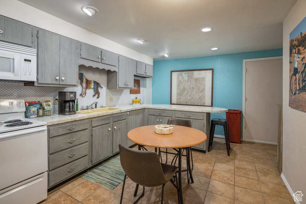 Kitchen featuring light tile floors, white appliances, gray cabinetry, kitchen peninsula, and tasteful backsplash