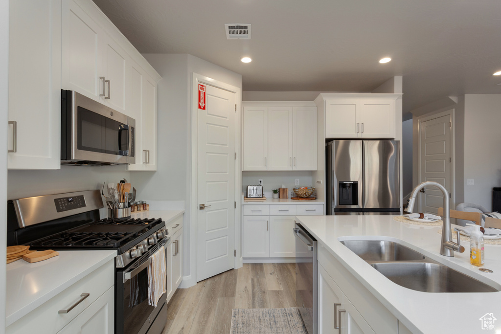 Kitchen featuring white cabinets, appliances with stainless steel finishes, light hardwood / wood-style flooring, and sink