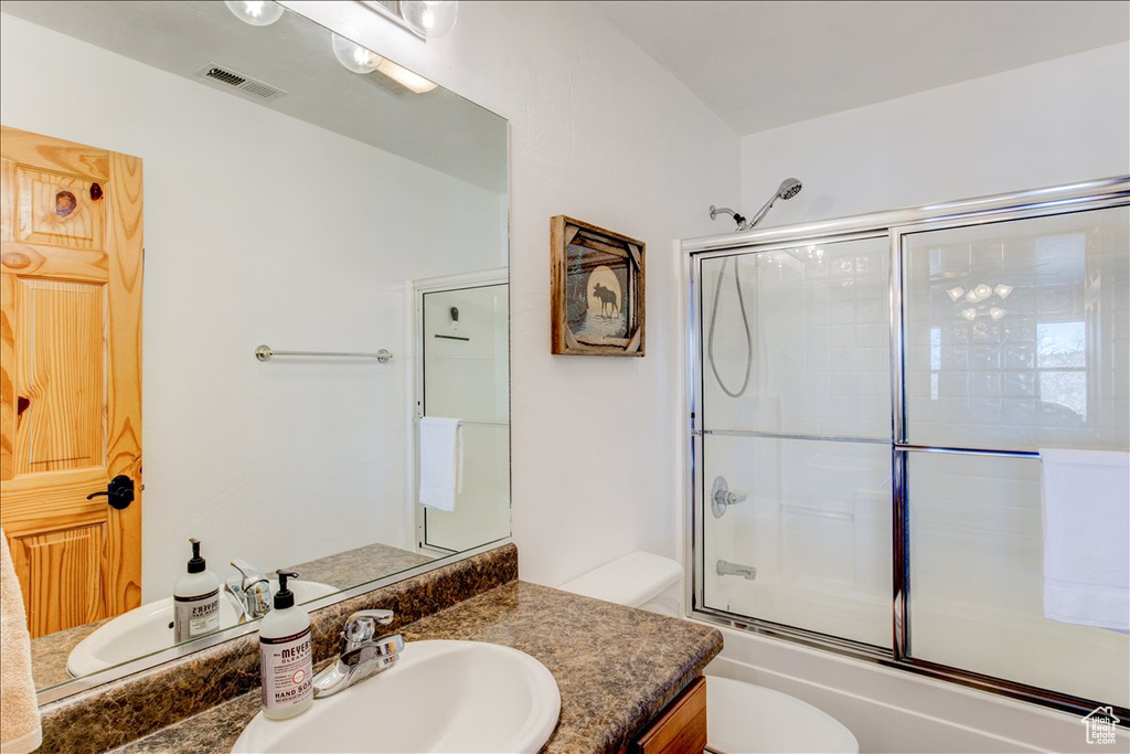 Full bathroom with toilet, large vanity, and enclosed tub / shower combo
