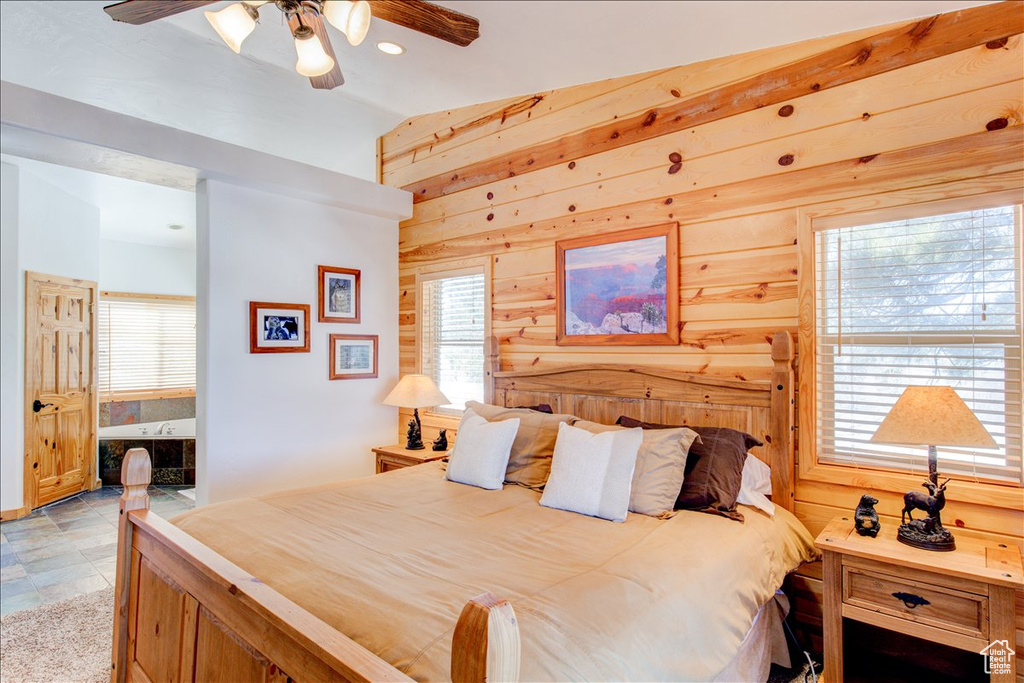 Bedroom with ceiling fan, light tile floors, multiple windows, and wood walls