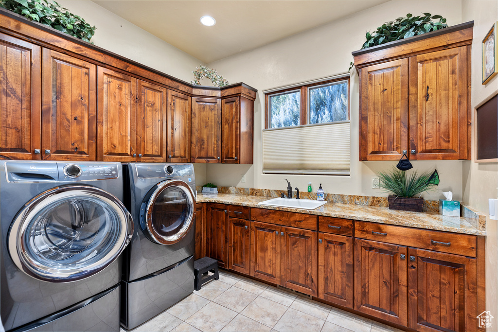 Clothes washing area featuring light tile floors, cabinets, washer and dryer, and sink