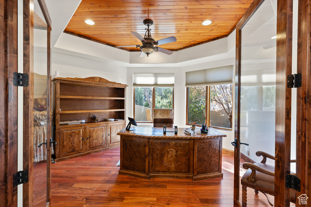 Home office with wood ceiling, dark wood-type flooring, a tray ceiling, and ceiling fan