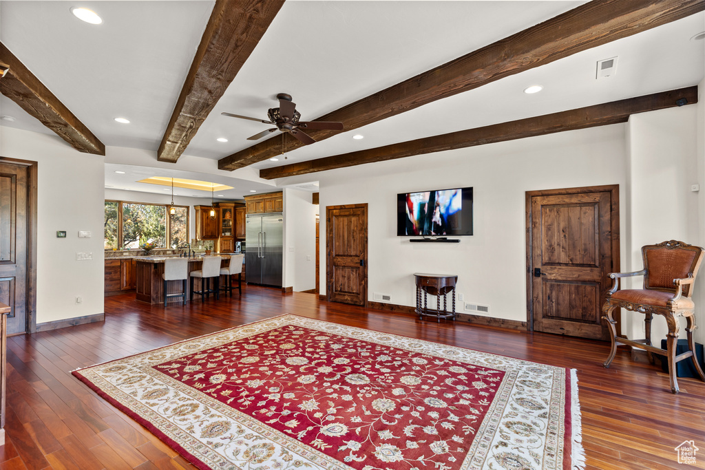 Living room featuring dark hardwood / wood-style floors, beam ceiling, and ceiling fan