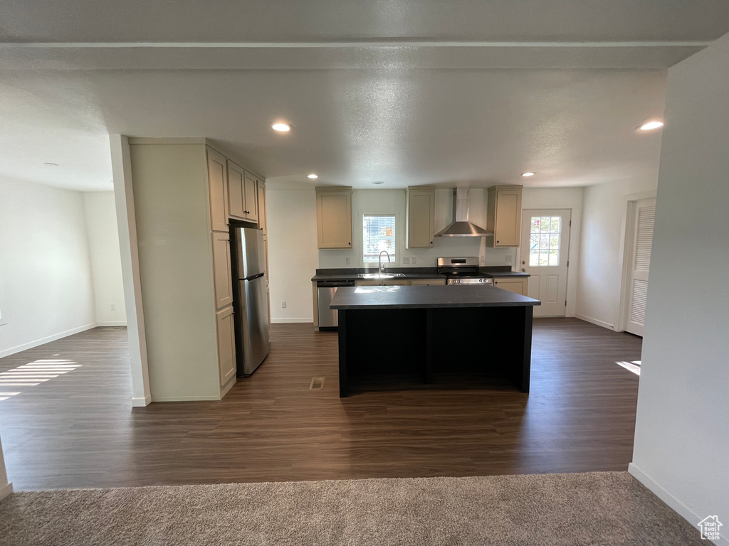 Kitchen featuring dark hardwood / wood-style flooring, a kitchen island, wall chimney range hood, sink, and appliances with stainless steel finishes