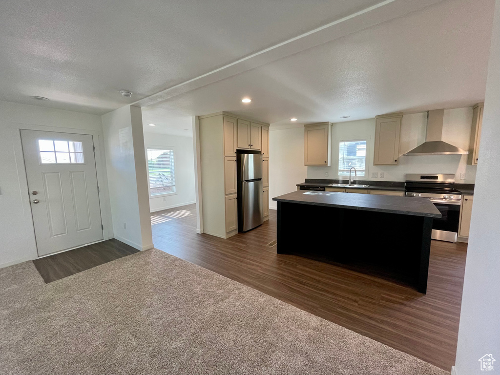 Kitchen with stainless steel appliances, dark wood-type flooring, wall chimney range hood, and a center island