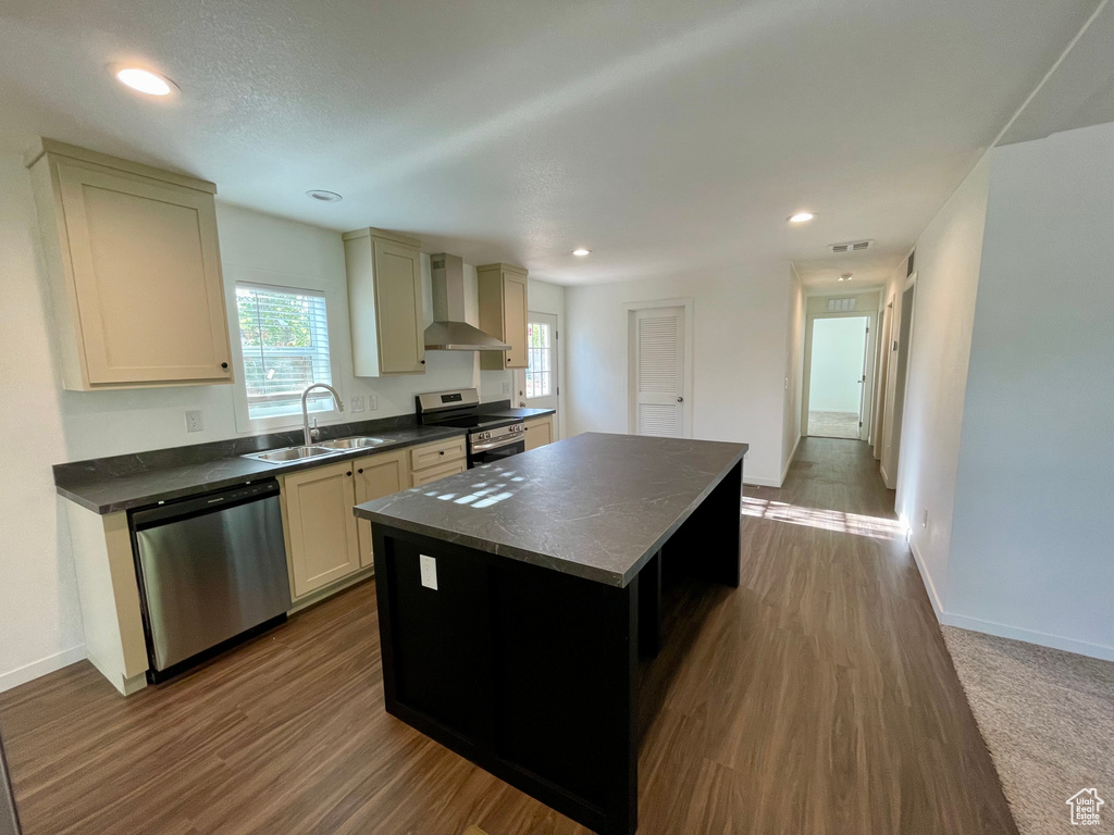 Kitchen featuring wall chimney range hood, dark hardwood / wood-style flooring, stainless steel appliances, a center island, and sink