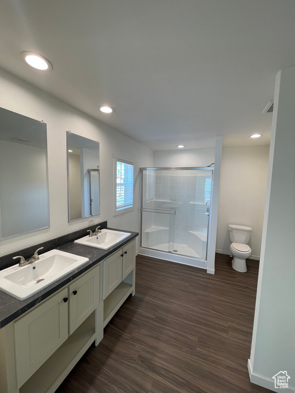 Bathroom featuring wood-type flooring, a shower with door, large vanity, toilet, and dual sinks