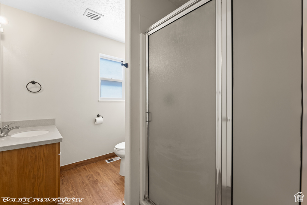 Bathroom featuring a textured ceiling, vanity, hardwood / wood-style floors, walk in shower, and toilet