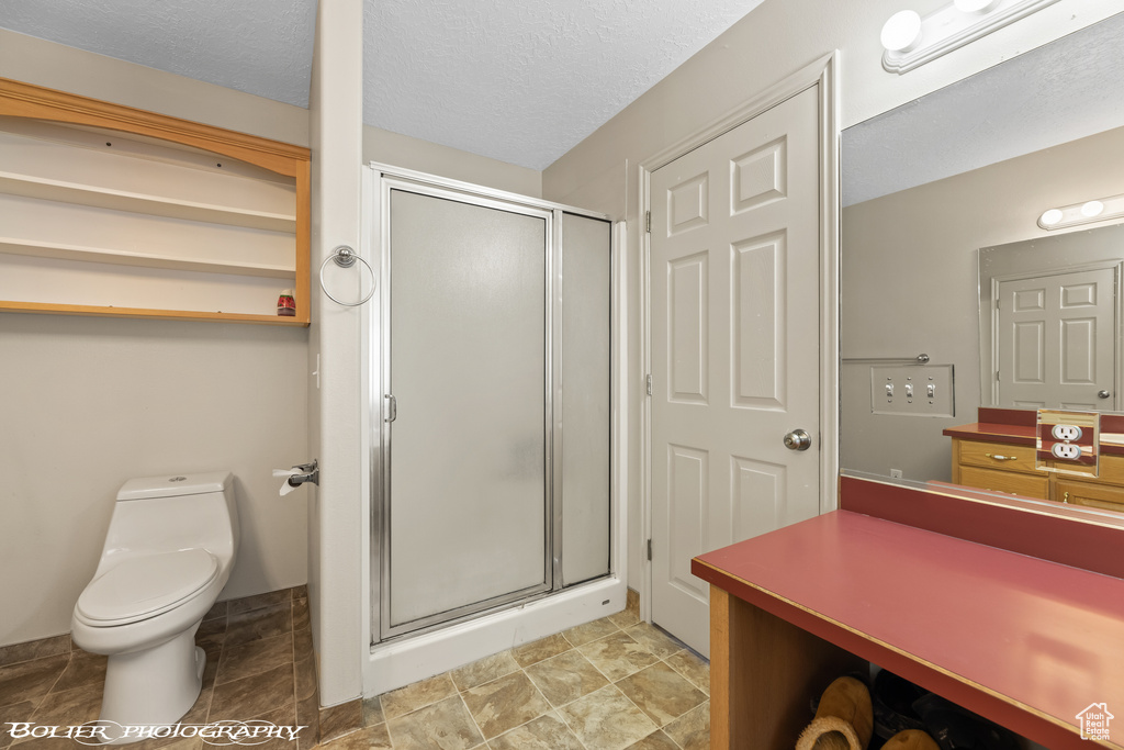 Bathroom with vanity, a textured ceiling, toilet, a shower with shower door, and tile flooring