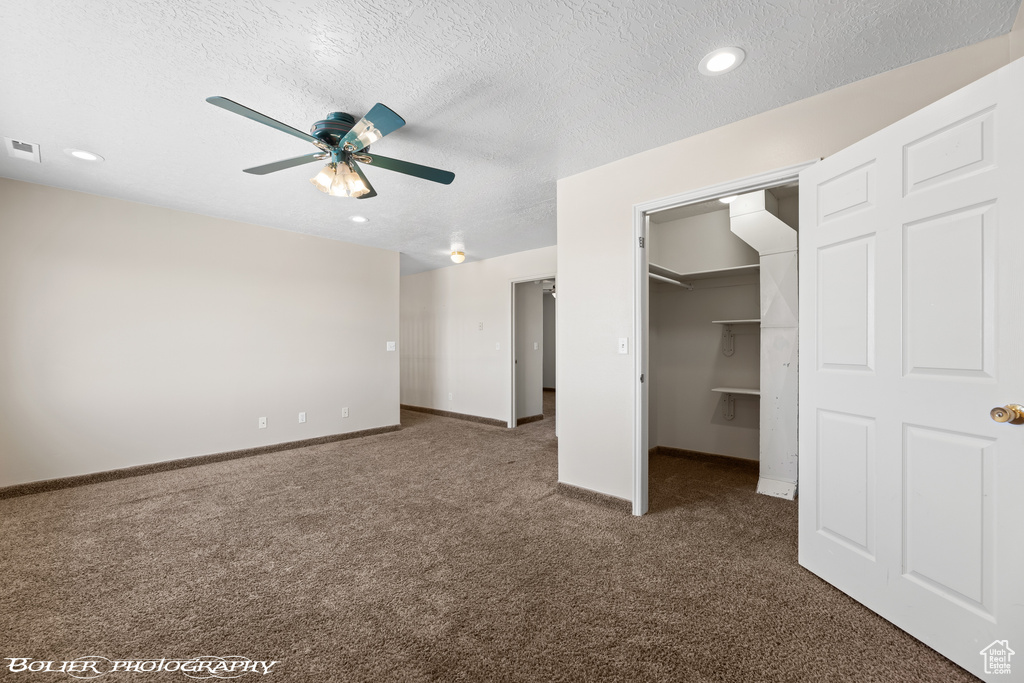 Unfurnished bedroom with a closet, a spacious closet, a textured ceiling, dark colored carpet, and ceiling fan