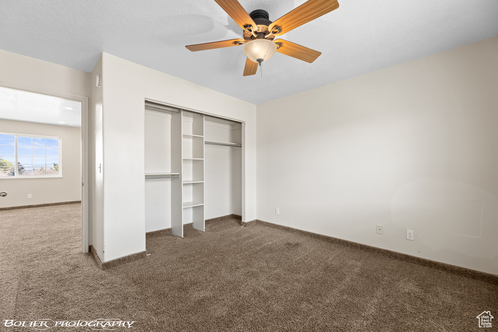 Unfurnished bedroom with dark colored carpet, ceiling fan, and a closet