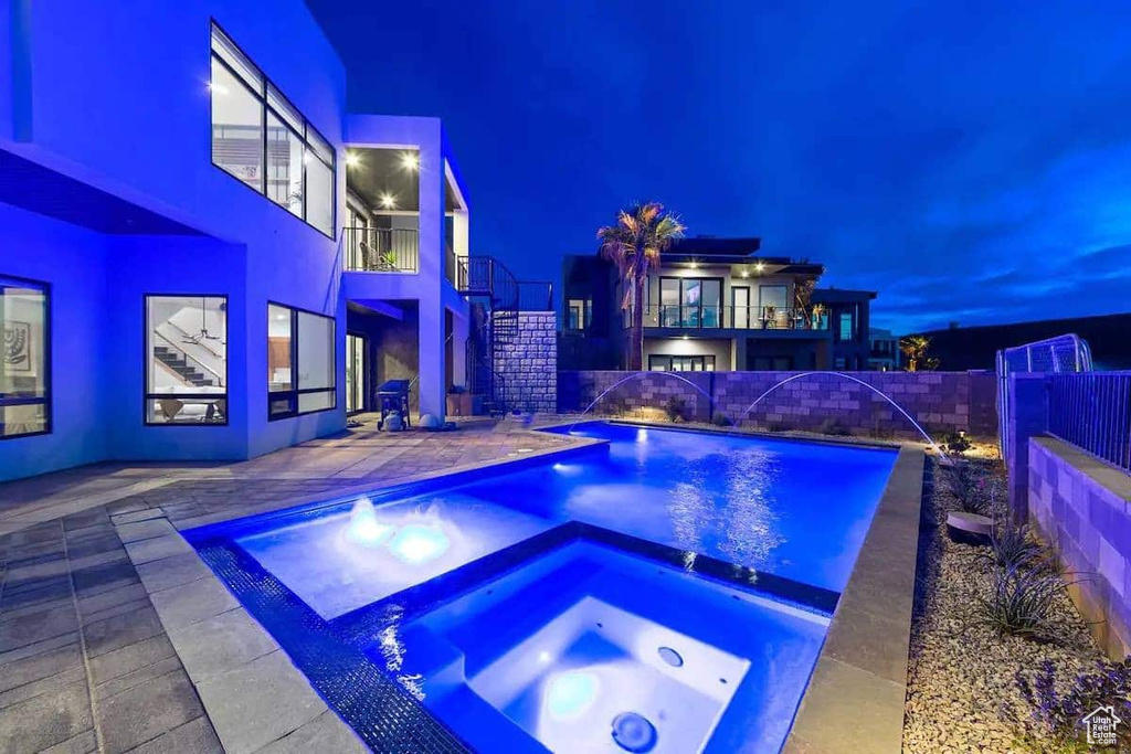 Pool at night with an in ground hot tub, a patio area, and pool water feature