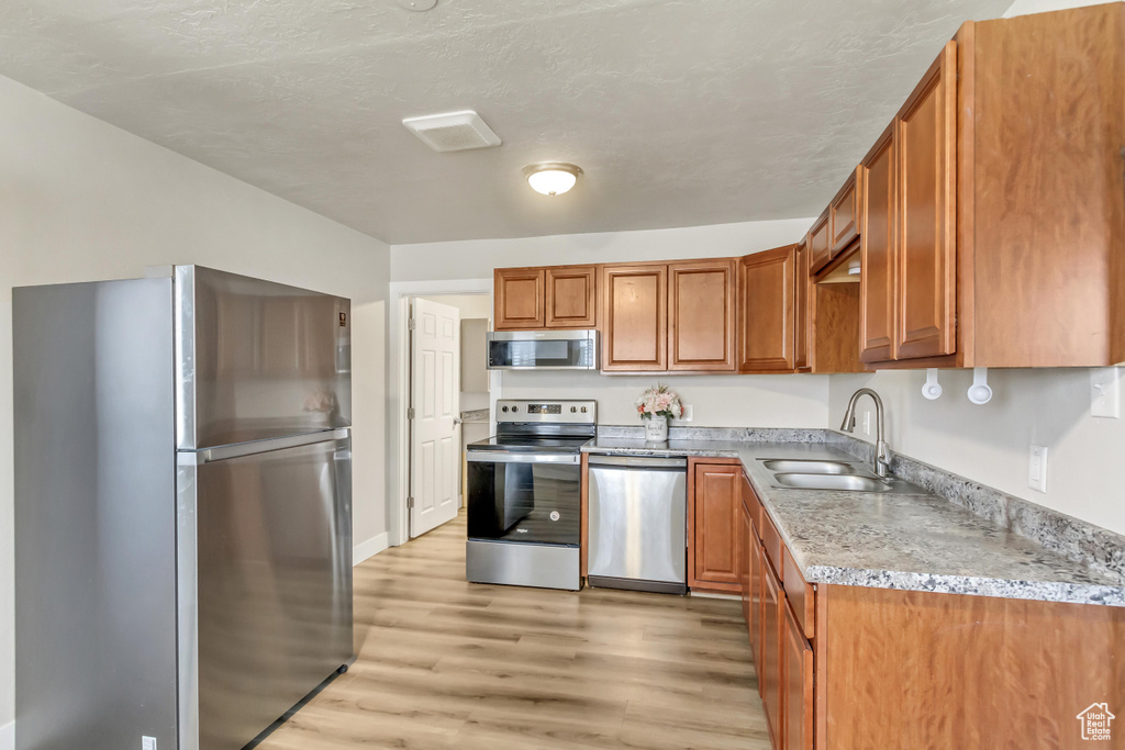 Kitchen with appliances with stainless steel finishes, light hardwood / wood-style flooring, light stone countertops, and sink