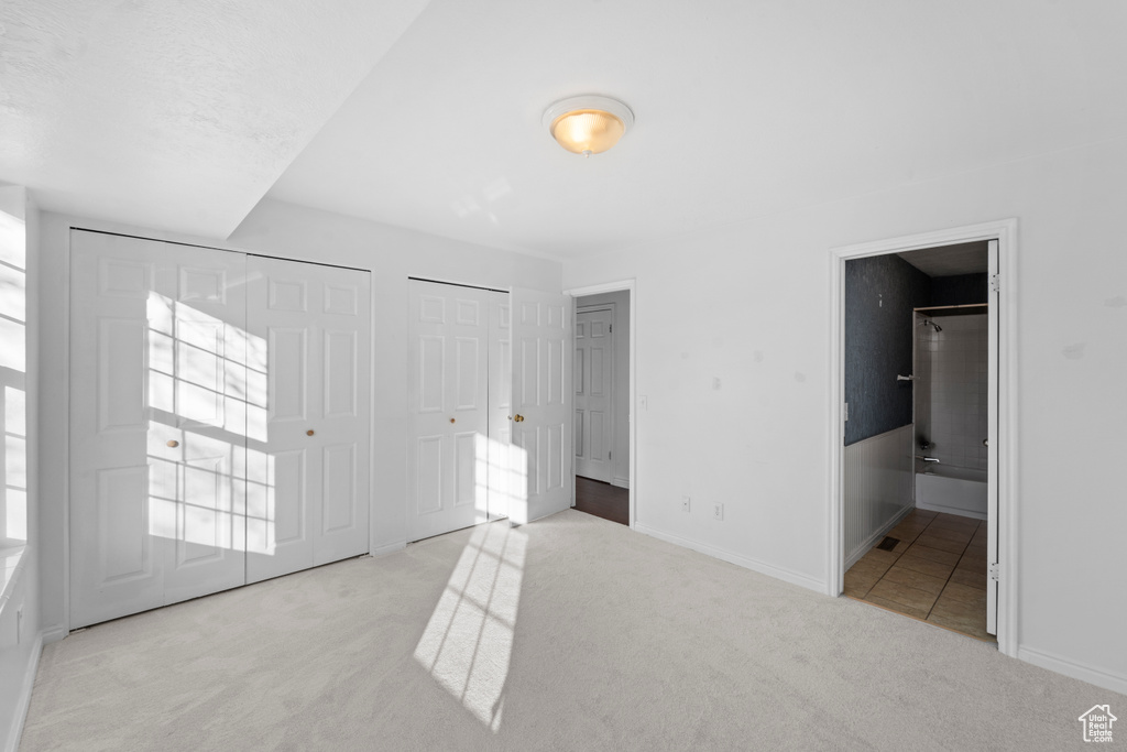 Unfurnished bedroom with multiple closets, light colored carpet, and ensuite bathroom