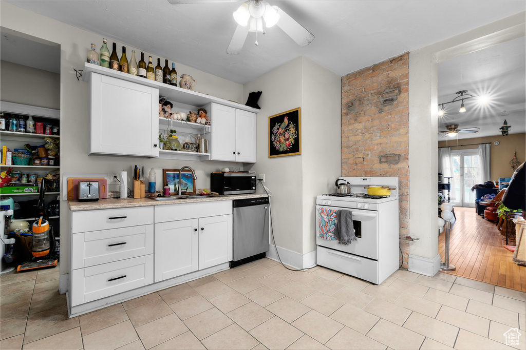 Kitchen with stainless steel appliances, brick wall, sink, light tile floors, and ceiling fan